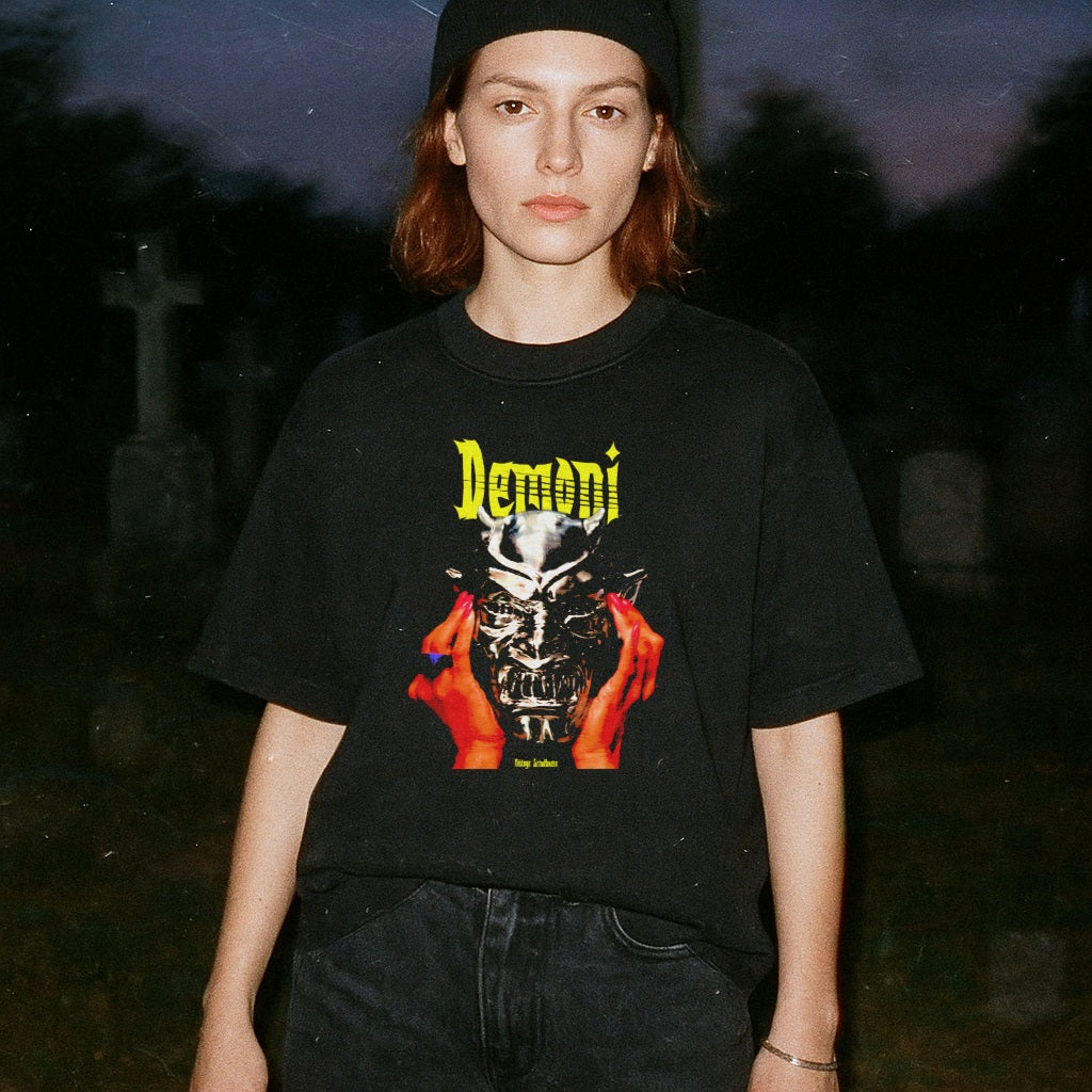 Person wearing a black t-shirt with a graphic design and text, standing in a dark outdoor setting.