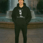 Man smiling wearing Night of the Living Dead Hoodie with black and white graphic standing by a city fountain