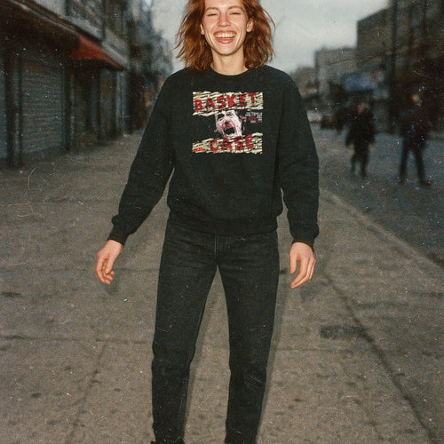 Woman standing outdoors wearing Basket Case sweatshirt with distressed screaming face graphic and torn text on black fabric