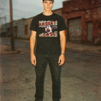 Person wearing a black t-shirt with graphic design standing on a street.