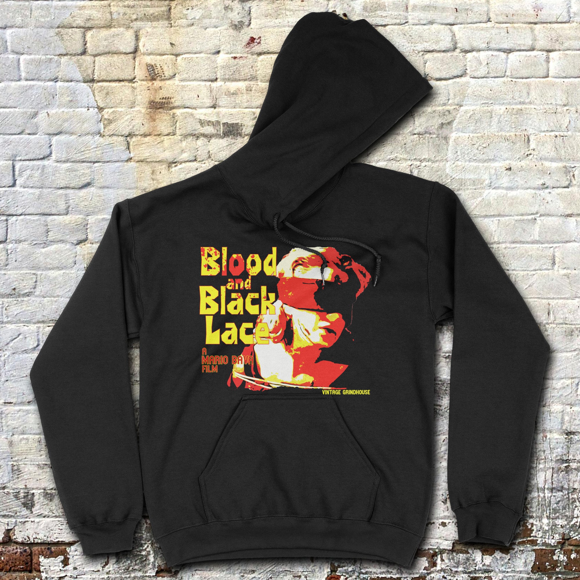 Black Blood and Black Lace hoodie with bold yellow and red vintage film graphic laid flat against brick wall background