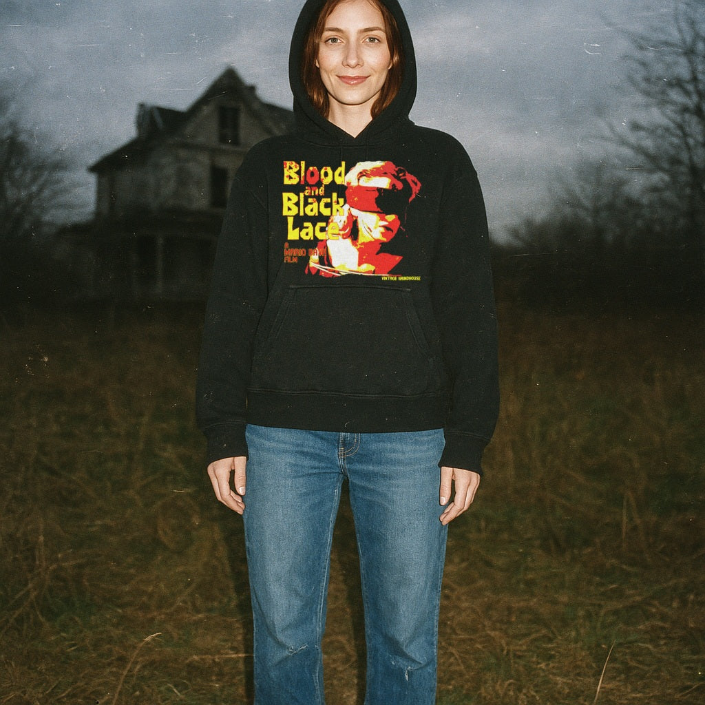 Person wearing Blood and Black Lace hoodie with vintage horror film graphic standing outdoors near old house at dusk