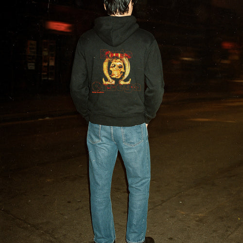 Person wearing a black hoodie with a graphic design on the back at night.