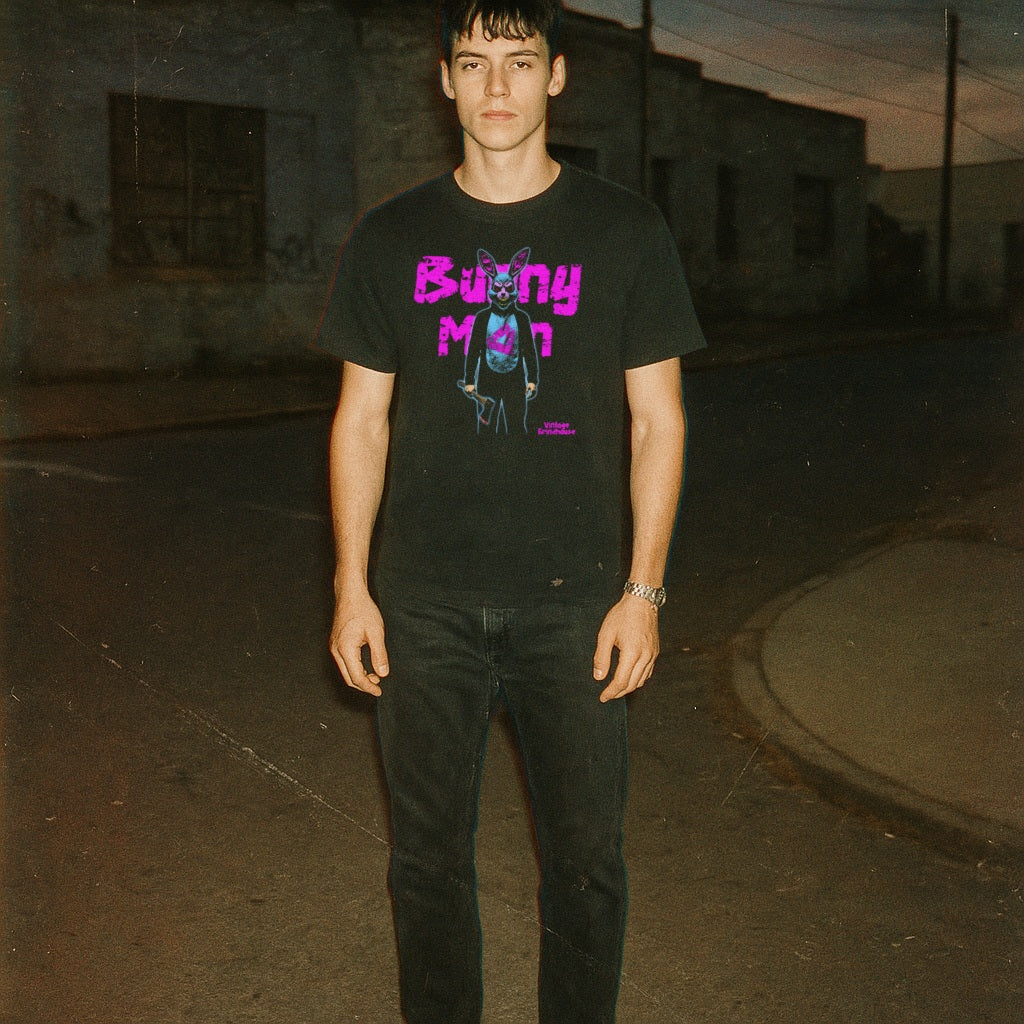 Man wearing black Bunny Man t-shirt with neon purple text and surreal bunny character standing on a dimly lit street at dusk