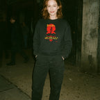 Woman wearing black Cannibal Holocaust sweatshirt with striking red and yellow graphic standing on dimly lit urban street at night