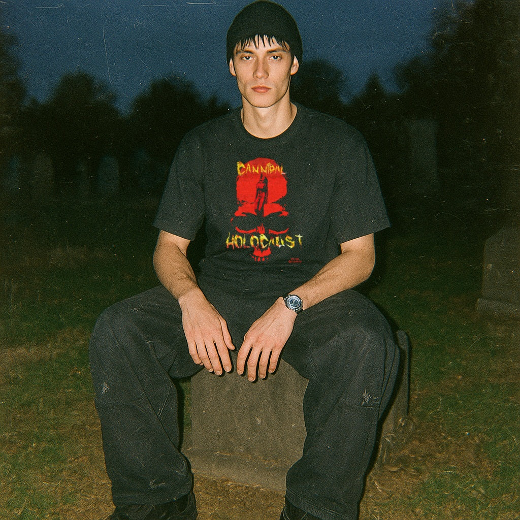 Model wearing black Cannibal Holocaust t-shirt with striking red and yellow graphic sitting outdoors at dusk