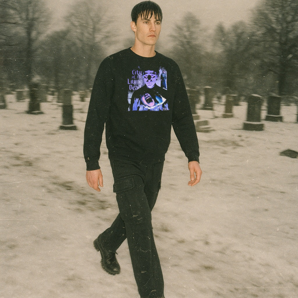 Model walking through snowy graveyard wearing City of the Living Dead sweatshirt with eerie bluish graphic on black fabric