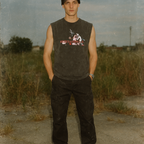Man wearing a sleeveless shirt with graphic design standing in an open field.