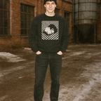 Man wearing Eraserhead sweatshirt with stylized black and white portrait and checkerboard pattern in rustic outdoor setting