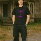 Man wearing black Edgar Allen Poe t-shirt with purple Gothic lettering standing outdoors by old wooden building