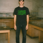 Person wearing black H.P. Lovecraft t-shirt with glowing green stylized text and cosmic tentacle design in dimly lit room