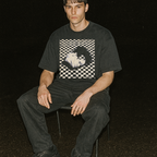 Person wearing a black t-shirt with a graphic design sitting against a dark background
