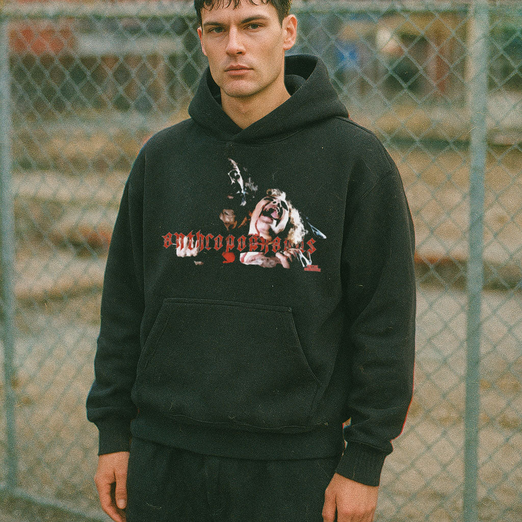 Person wearing a black hoodie with graphic design in front of a chain-link fence.