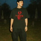 Man standing in dark cemetery wearing black The Burning t-shirt with distressed red graphic and text design