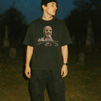 Male model wearing Zombi 2 t-shirt with eerie decayed zombie face and cityscape under dark night sky