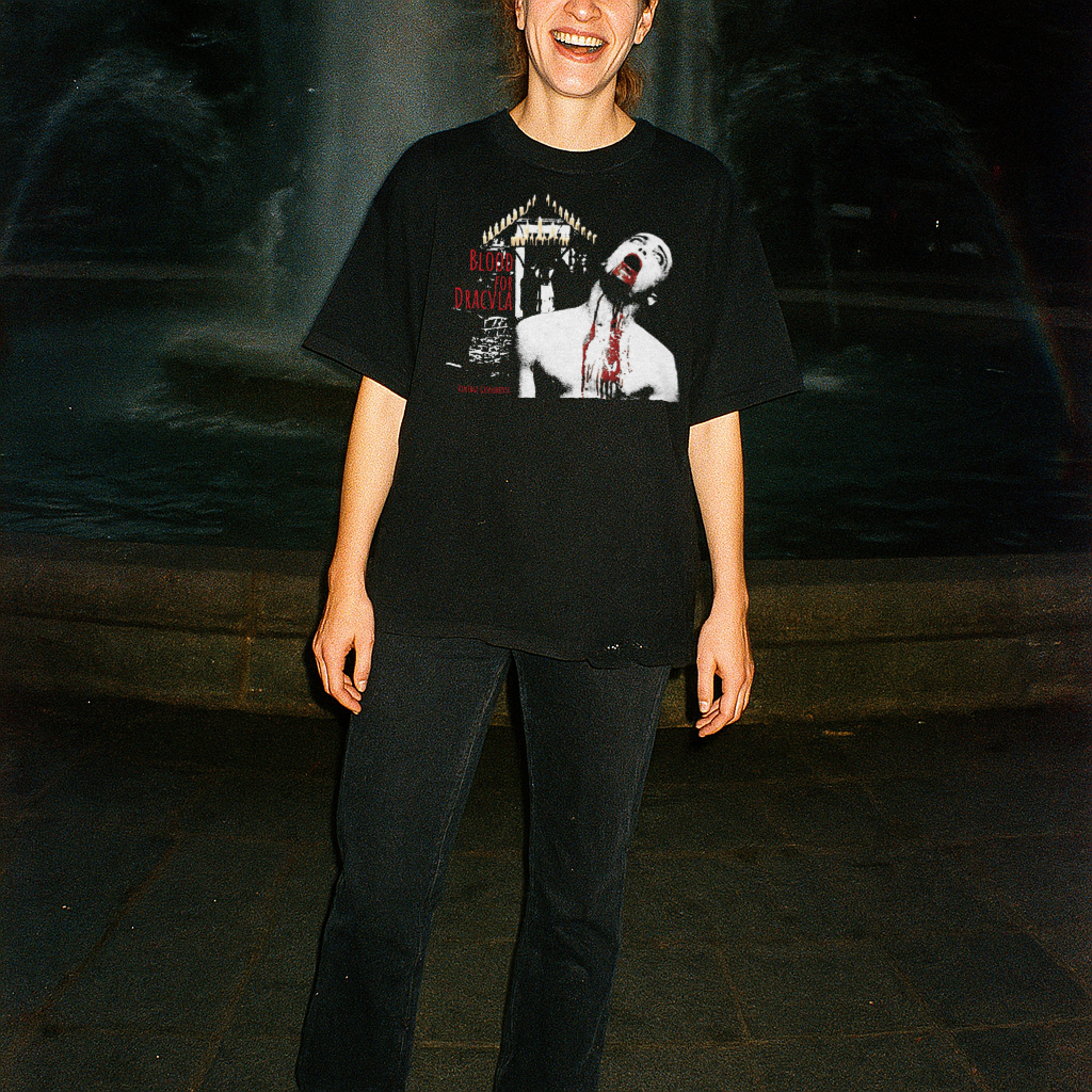 Person wearing a black t-shirt with graphic design, standing in front of a fountain at night.