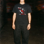Person wearing a black t-shirt with graphic design in a dark alleyway