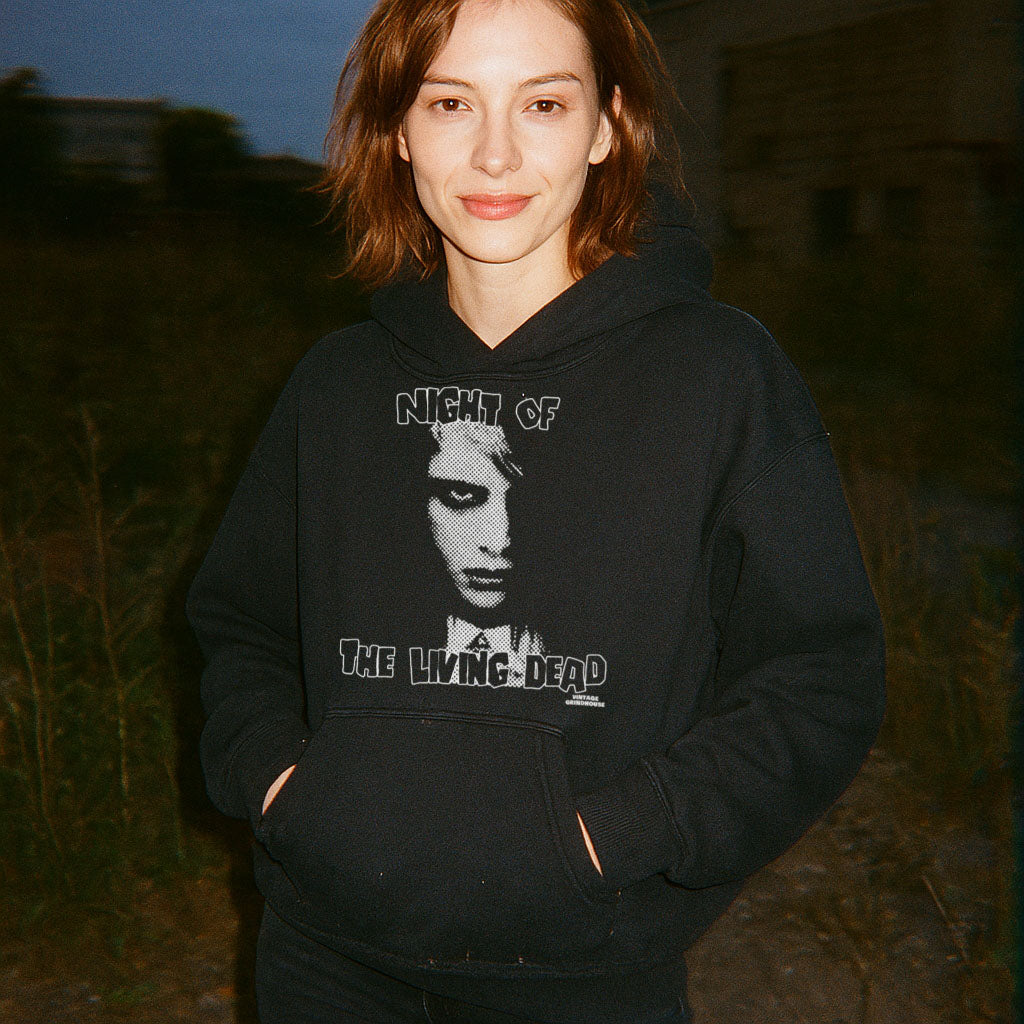 Woman wearing Night of the Living Dead Hoodie featuring a black and white eerie face graphic on dark fabric outdoors at dusk