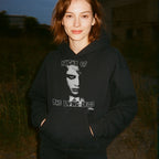 Woman wearing Night of the Living Dead Hoodie featuring a black and white eerie face graphic on dark fabric outdoors at dusk