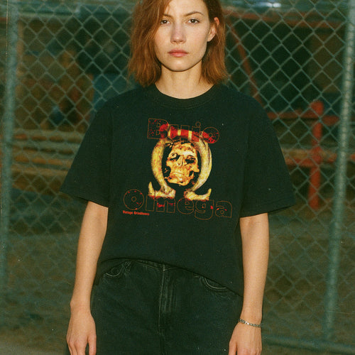 Person wearing a black t-shirt with a graphic design in front of a chain-link fence.