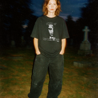 Model wearing Night of the Living Dead t-shirt with ghostly face design standing in dimly lit cemetery background