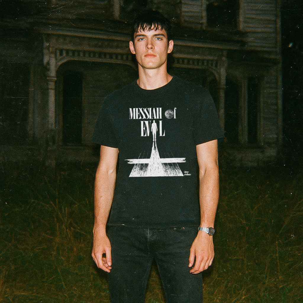Male model wearing Messiah of Evil - Edition Black shirt with white graphic and text in front of a dark, eerie house