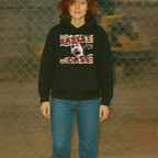 Person wearing a black hoodie with graphic design in front of a chain-link fence.