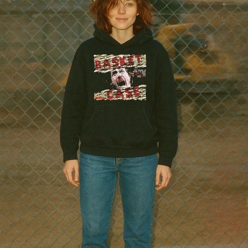 Person wearing a black hoodie with graphic design in front of a chain-link fence.