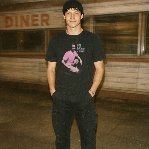 Young man in black beanie wearing an Ed Wood t-shirt with vintage style graphic standing by a diner at night