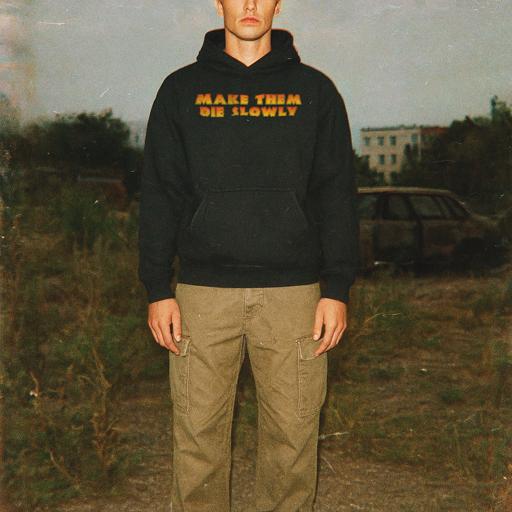 Person wearing a black hoodie with 'MAKE THEM DIE SLOWLY' text in a natural setting.