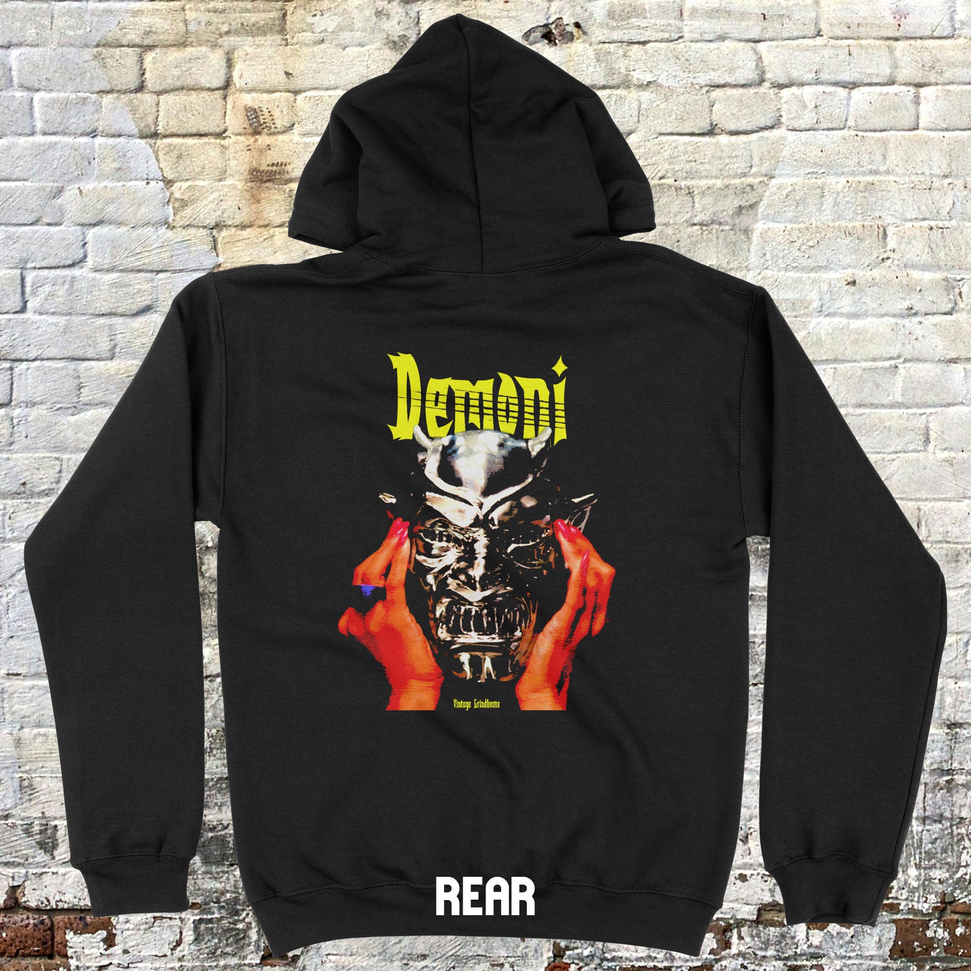 Demoni hoodie (rear print) with detailed horror mask graphic held by hands and yellow stylized text on black fabric