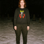 Person standing outdoors at night wearing Demoni aka Demons sweatshirt with bold yellow text and fiery red hands graphic