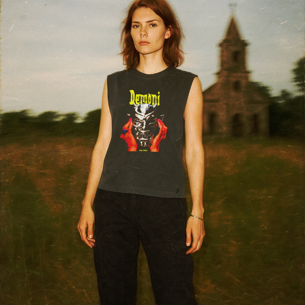 Demoni muscle tank worn by model with graphic of metallic skull held by red hands and bold yellow text on dark fabric