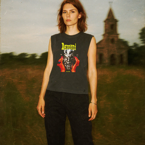 Woman wearing Demons aka Demoni muscle tank with bold yellow text and striking graphic of demonic figure and red hands on dark fabric