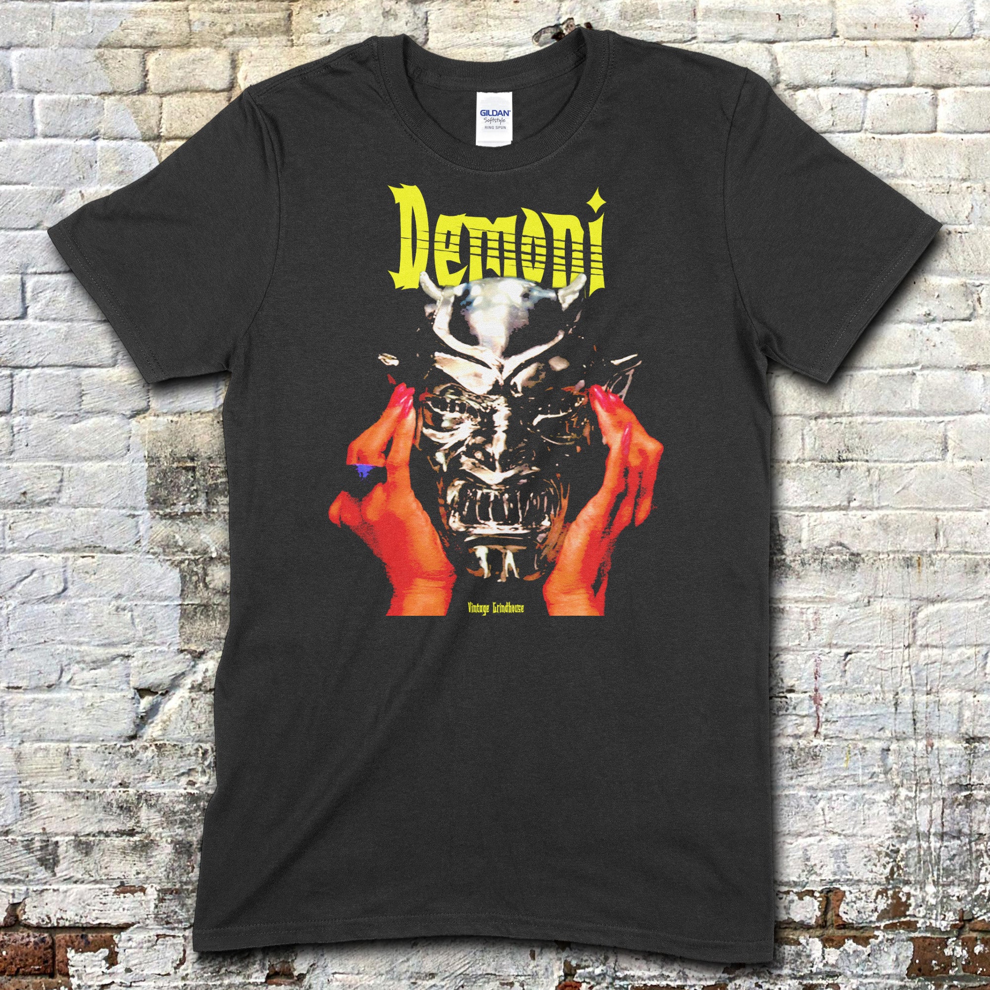 Black t-shirt featuring a graphic of hands holding a demonic silver mask with Demoni text in yellow on front