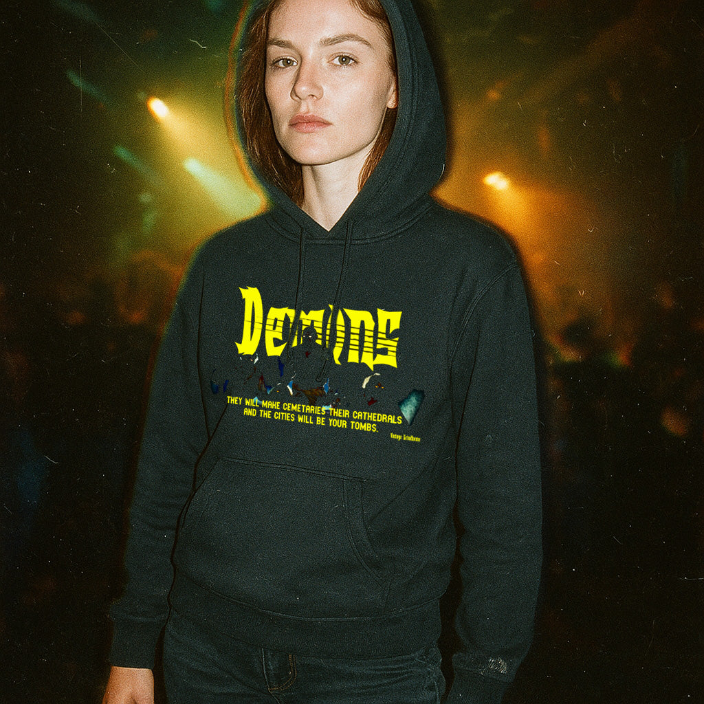 Person wearing Demons hoodie with bold yellow gothic text and dark graphic print in dimly lit atmospheric setting