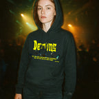 Person wearing Demons hoodie with bold yellow gothic text and dark graphic print in dimly lit atmospheric setting