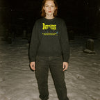 Person standing in snowy graveyard wearing Demons aka Demoni sweatshirt with bold yellow text and dark graphic on black fabric