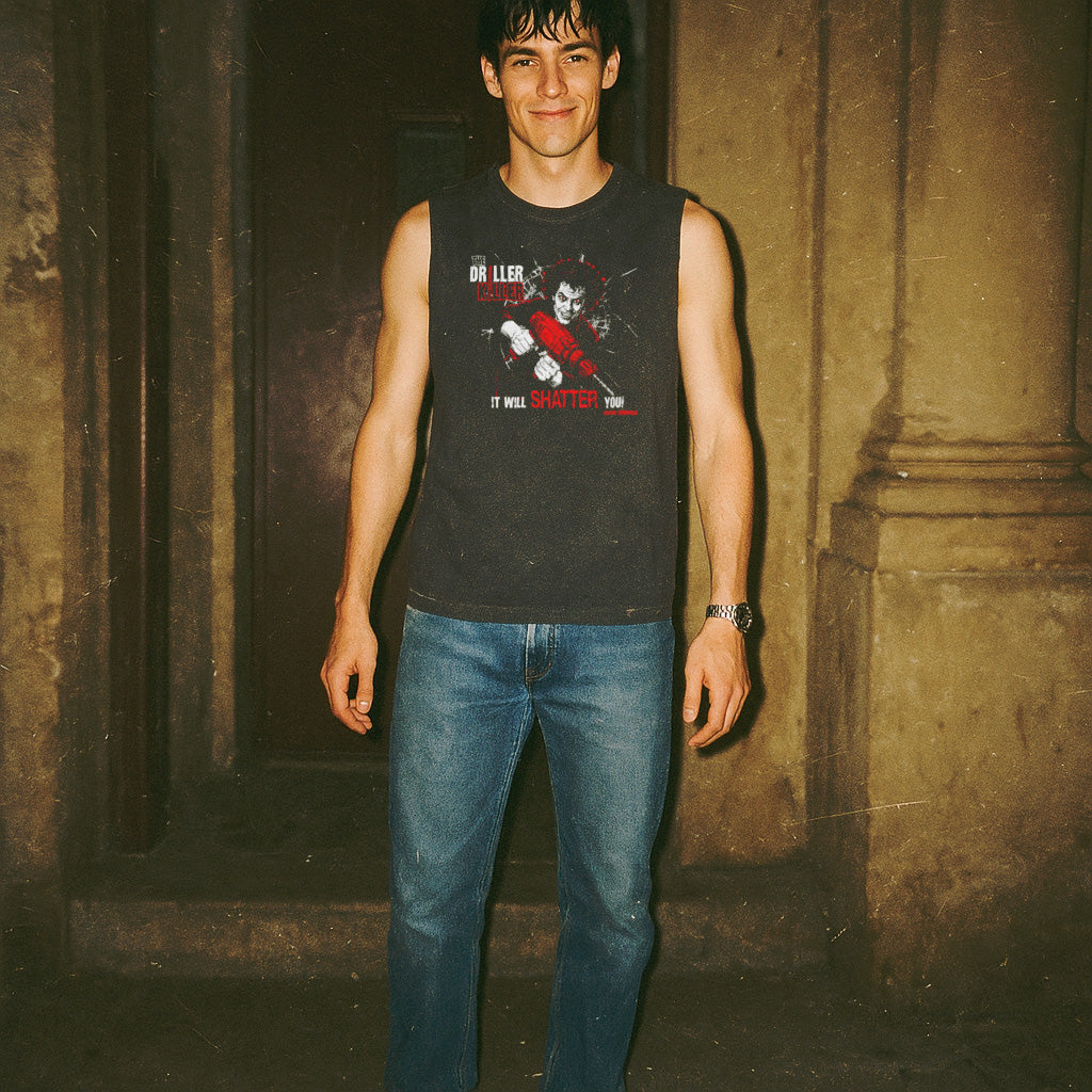 Man wearing a black sleeveless shirt with graphic design and blue jeans standing against a textured wall.