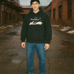 Person wearing Eraserhead Baby hoodie with monochrome surreal graphic standing in urban alley with brick buildings in background