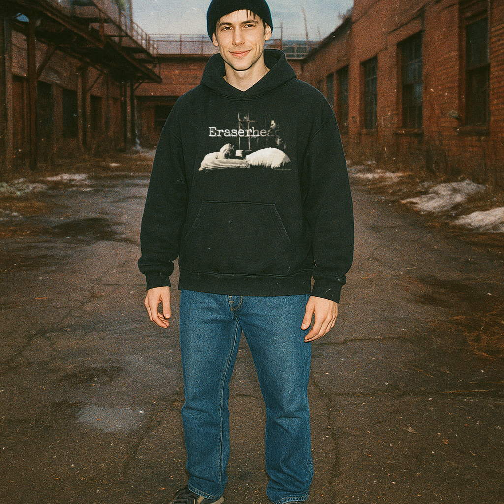 Person wearing Eraserhead Baby hoodie with monochrome surreal graphic standing in urban alley with brick buildings in background