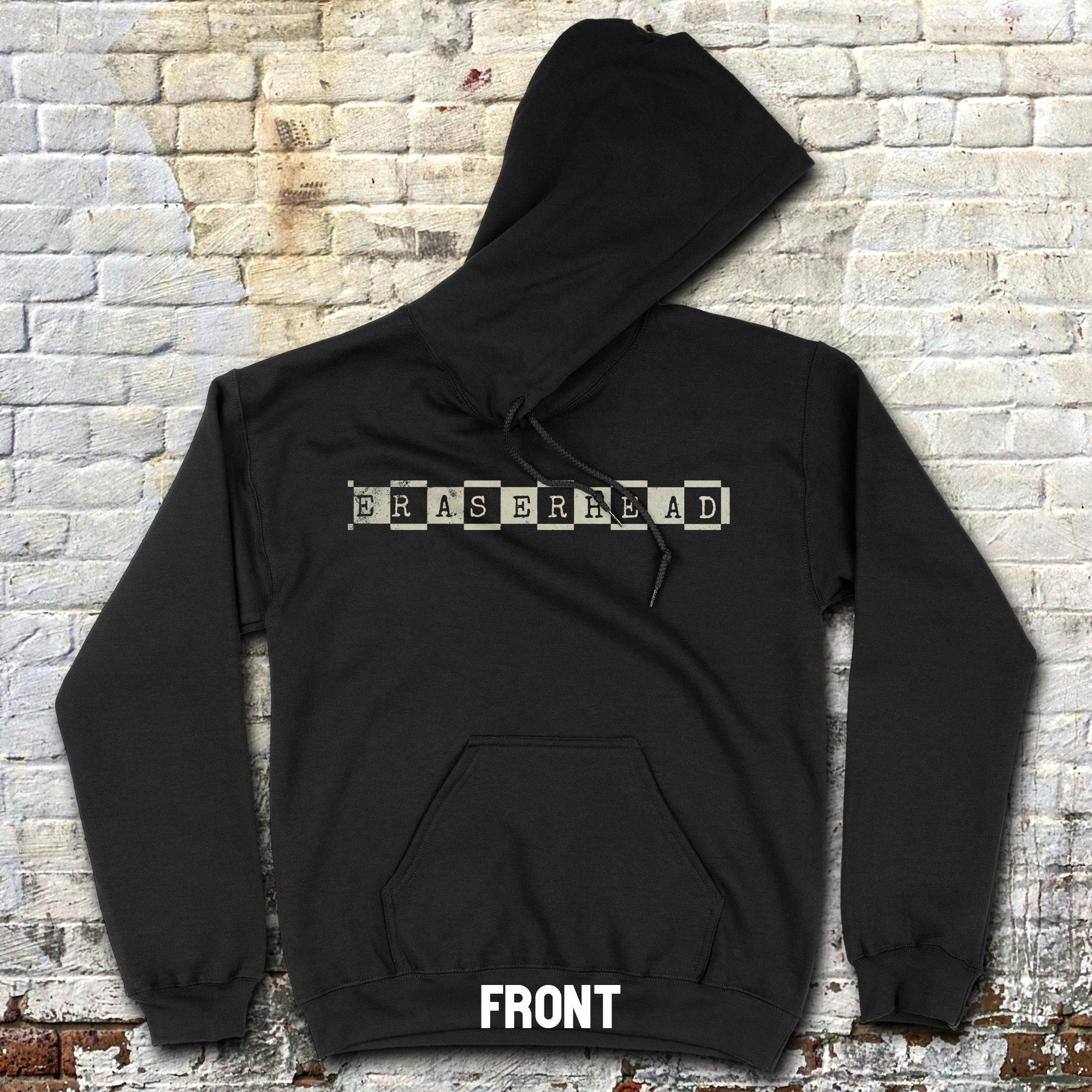 Black hoodie displaying Eraserhead - front and rear prints! with typewriter-style text on front laid flat on textured brick floor