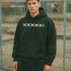 Person wearing a black hoodie with 'ERASHERHEAD' text in front of a chain-link fence.