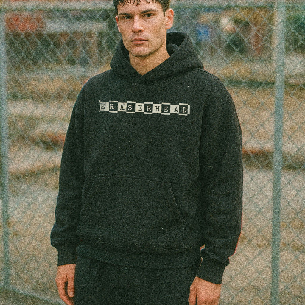 Person wearing a black hoodie with 'ERASHERHEAD' text in front of a chain-link fence.