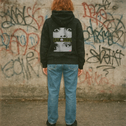 Person wearing a black hoodie with a graphic design in front of a graffiti-covered wall.