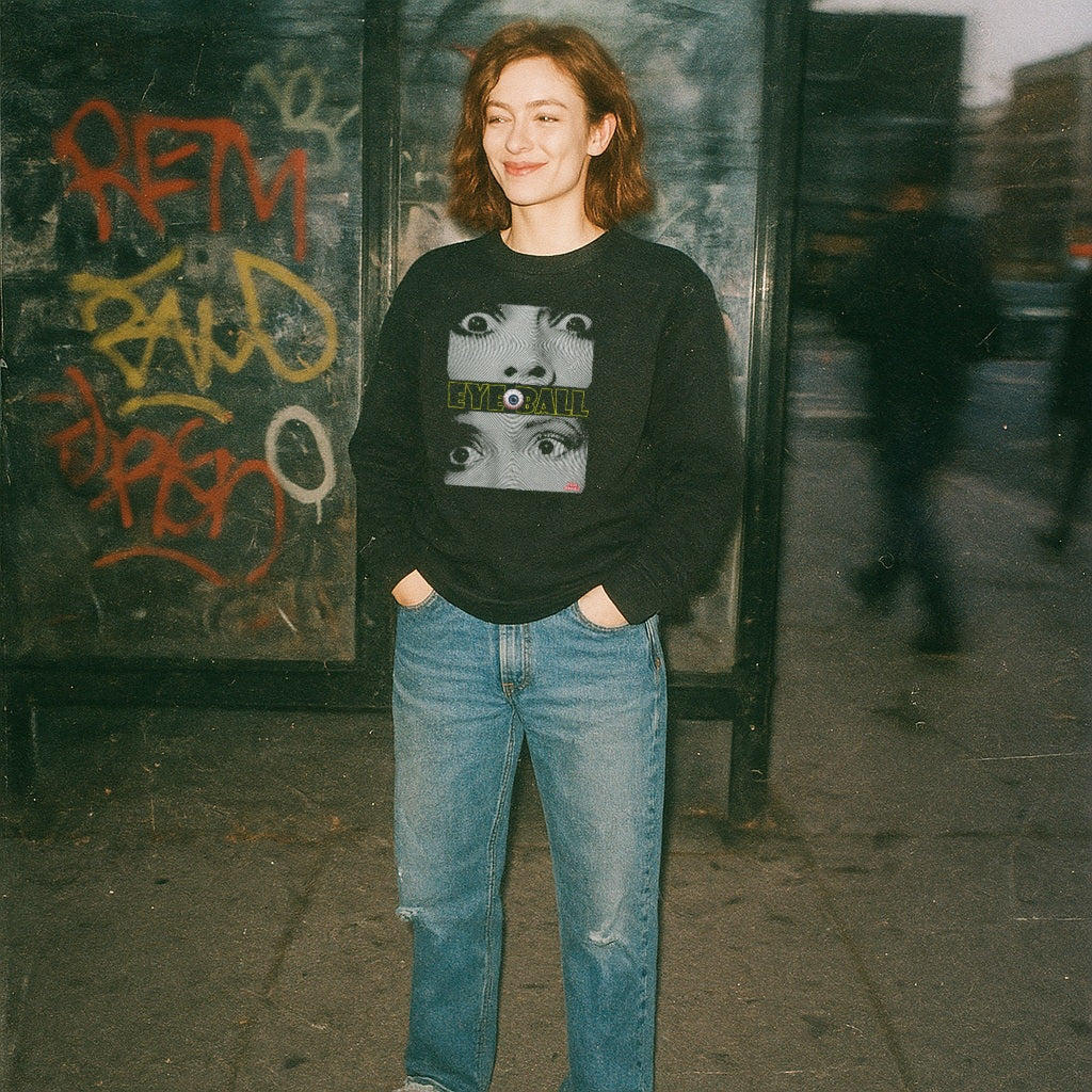 Person wearing Eyeball sweatshirt with graphic of multiple eyes and distinct central eyeball on black fabric outdoors