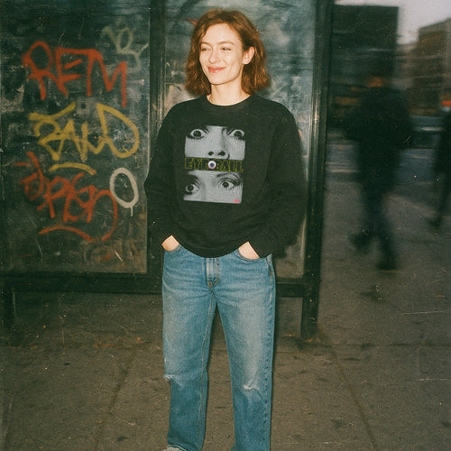 Person wearing Eyeball sweatshirt with graphic of multiple eyes and distinct central eyeball on black fabric outdoors
