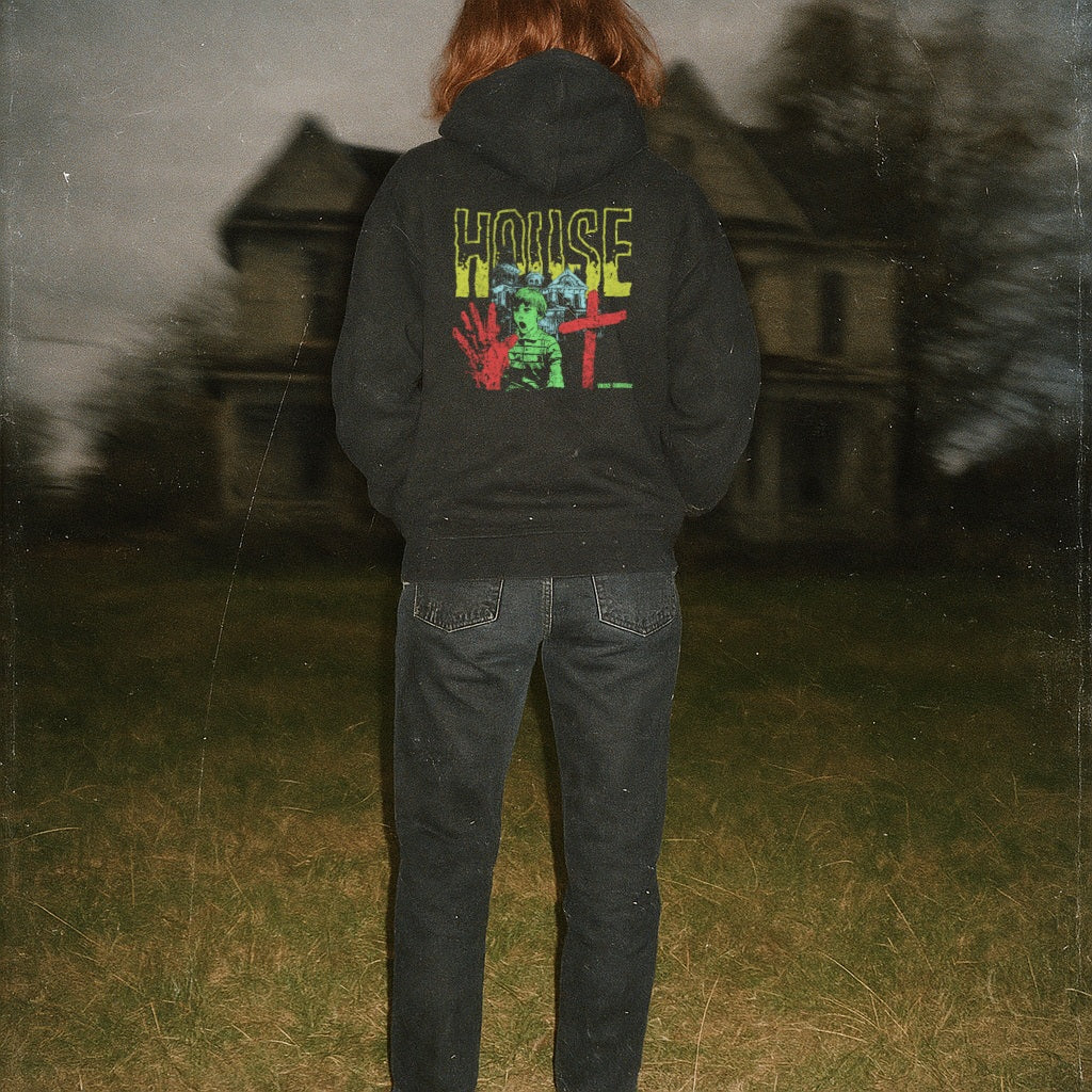 Person standing in front of dark house wearing black House hoodie (rear print) with colorful eerie graphic on back