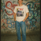 Person wearing a graphic t-shirt in front of a graffiti-covered wall
