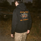 Person wearing a black hoodie with a graphic design on the back, standing outdoors.